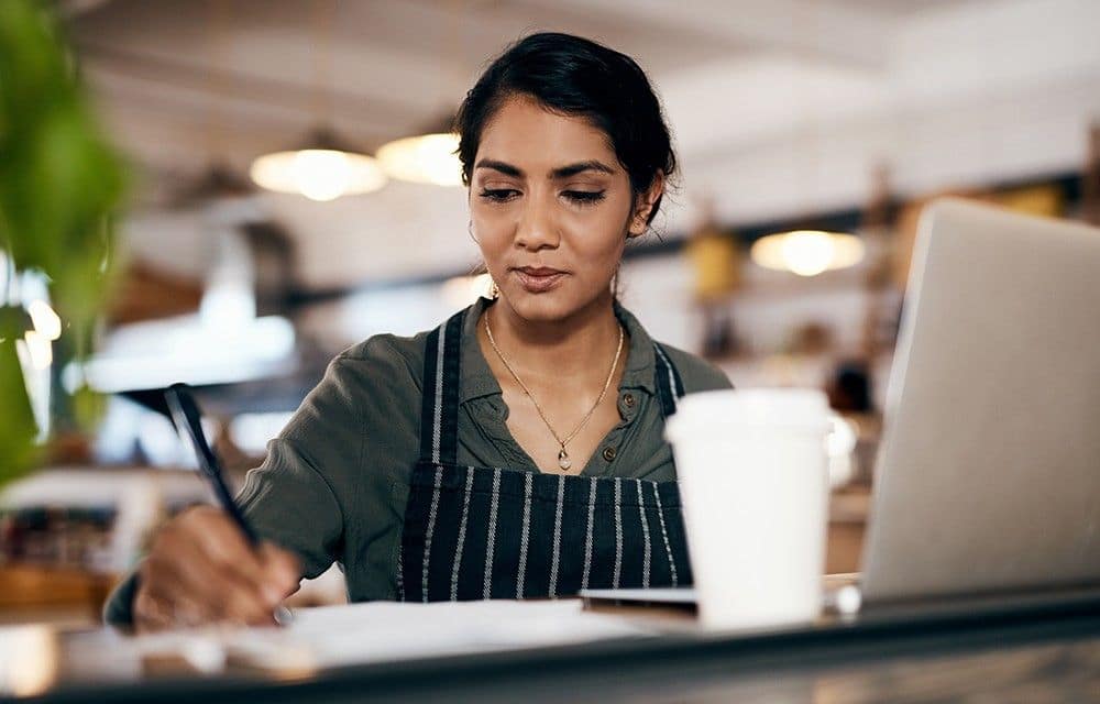 Young lady writing with pen something in front of laptop